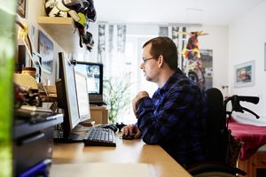 Ein Mann im Rollstuhl sitzt vor dem Computer und schaut konzentriert in den Bildschirm.